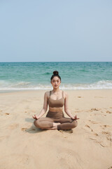 Fototapeta na wymiar Young woman meditating on beach in the morning