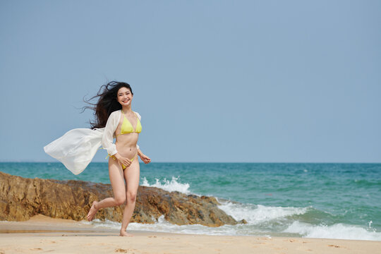 Happy young woman in yellow bikini jogging on sea beach in the morning