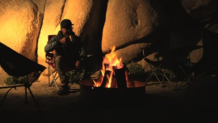 African-American young traveler man enjoying nature, drinking hot tea from mug cup near bonfire at summer campsite. Enjoying camping fire and celebrating 4th of July, 4K slow-mo