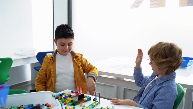 Robotics programming class. Children construct and code Robot. STEM education using constructor blocks and laptop tablet, remote control joystick. Technology educational development for school kids