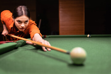 Fototapeta premium Woman with cue aiming at billiard ball at table, gambling. American pool billiard. Fragment of the pool billiard game in process. Copy space