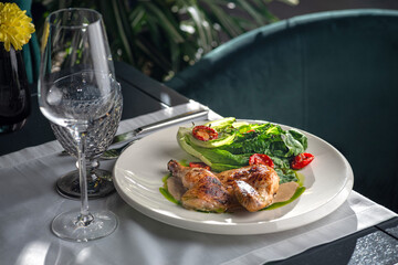 Half of a roasted chicken, on plate with herbs and tomatoes.