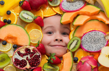 Fototapeta na wymiar Funny fruits. Happy smiling kid smiling face portrait surrounded by fruits. Kids face are peeking out of the mix fruits.