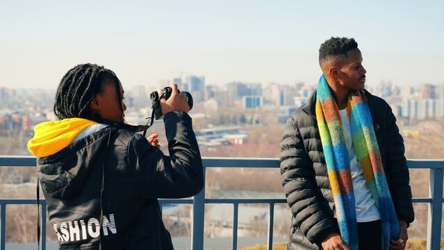 Beautiful young african american tourist woman posing in front of male friend taking photos