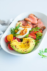 Keto breakfast of salmon, eggs, avocado and nuts on white plate, white background.