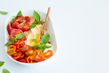 Hummus with tomatoes, peppers, basil and olive oil in white plate, white background.