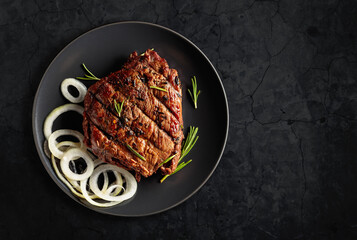 Grilled ribeye beef steak with rosemary and marinated onion on a black stone table. - obrazy, fototapety, plakaty