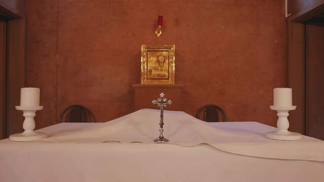 Altar covered with white cloth with silver crucifix and candles against the wall with golden icon