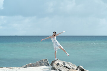 A beautiful girl stands on the rocks near the sea, sea summer land, woman tourist standing on the rock of sea in summer