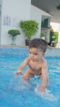 Happy smiling kid playing in the swimming pool. Cute baby boy splash the water enjoys summer  vacation. Funny little caucasian child toddler having fun in outdoor nature on sunny day. Vertical video.