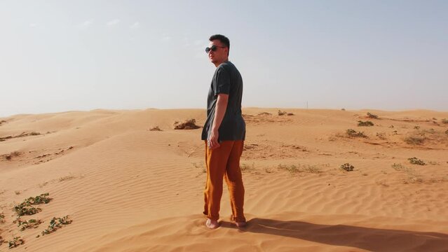 Young man stands barefoot in desert and looks around. Back view. Concept of contemplation and relaxation. Slow motion