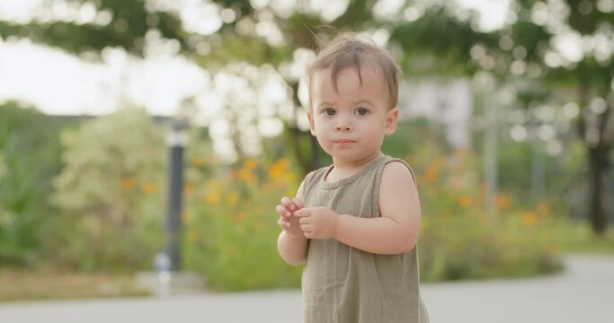 Adorable little happy smiling kid playing in the park. Slow Motion portrait shot of cute baby girl looking at camera. Active caucasian child learning to explore outdoor nature on sunny spring day. 
