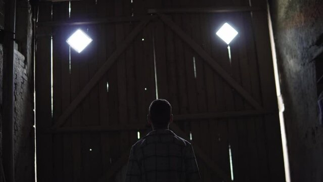 Static view of a boy waiting in front o fa large wooden barn door