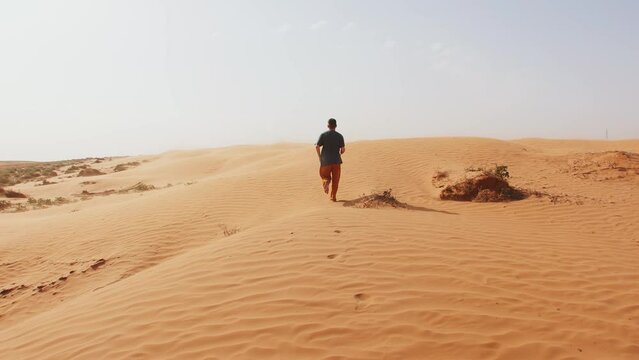 Young man runs barefoot on sandy hill in desert. Slow motion