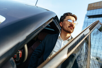 Young handsome businessman in a suit comes out of the luxury car