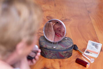 Mature woman reflected in mirror applying a makeup at home.
