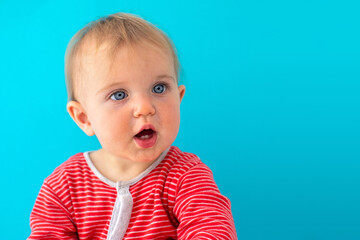 Sweet baby girl closeup portrait of child looks away surprised isolated on blue background, cute...