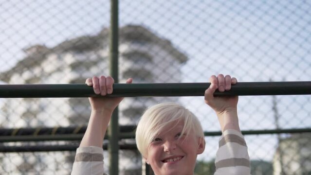 A blonde boy pulls himself up on the crossbar on the street.