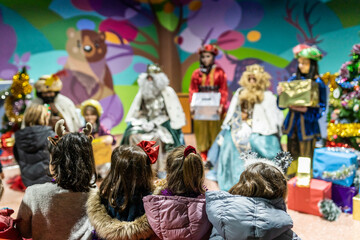 The three kings visiting children in a children's school, christian tradition, christmas festival in school, unrecognizable people, the background out of focus.