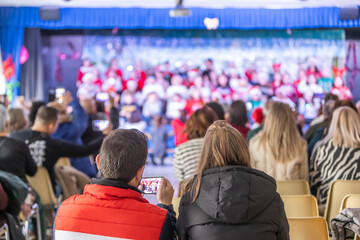 Families enjoying the Christmas festival at their children's school, father videotaping with his...