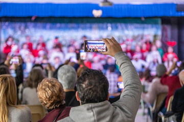 Families enjoying the Christmas festival at their children's school, father videotaping with his phone, unrecognizable people and out-of-focus background