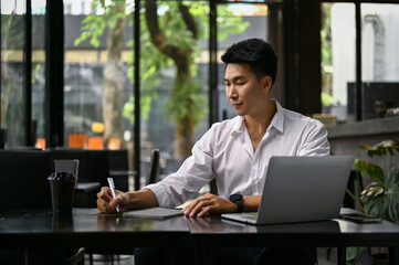 Successful businessman writing something on paper, remote working at a coffee shop