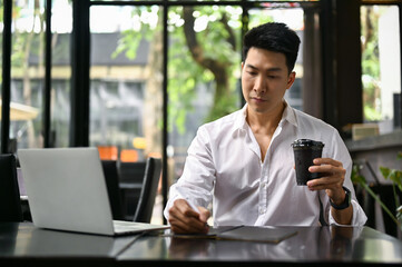 A businessman taking notes on his notebook while having afternoon coffee at a coffee shop.