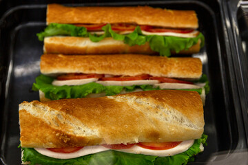 Vegetarian baguette stuffed with cheese, herbs and tomatoes on the counter in the store. Fast popular food. Close-up.