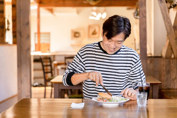 Fototapeta premium ランチ・昼食にカフェでハンバーガーをフォークとナイフで食べる男性 