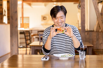 お昼休みにカフェやレストランでハンバーガーを食べるアジア人の男性
