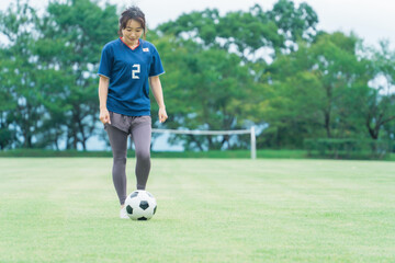 サッカー場でユニフォームを着てサッカー・フットサルの練習をする日本人女性
