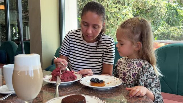 Mom feeds little girl French cake choux with craquelin dough in cafe