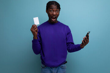 surprised joyful african young man with dreadlocks holding smartphone