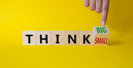 Think Big vs Small symbol. Businessman Hand points at wooden cubes with words Think Small and Think Big. Beautiful yellow background. Business and Think concept. Copy space