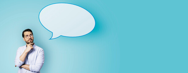 Attractive young european businessman with speech bubble on wide blue background. Opinion, speech and communication concept. Mock up place.