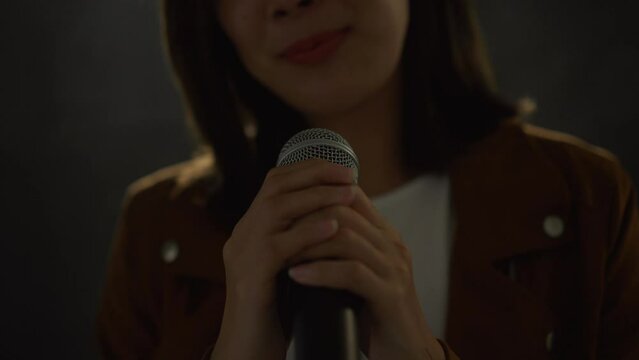 Close-up microphone Attractive singer woman singing music on stage with spotlight strike through the darkness at concert event. Beautiful female musician performing live with light and smoke at hall.