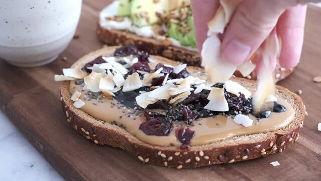 Cooking vegan breakfast toast with peanut butter, jam and coconut on wooden board.