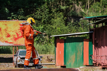 A firefighter is standing sideways and holding an iron ax in an outdoors location.