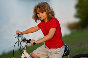 Obraz premium Child on bicycle. Boy in a helmet riding bike. Little cute caucasian boy in safety helmet riding bike in city park. Child first bike. Kid outdoors summer activities. Kid on bicycle. Boy ride a bike.