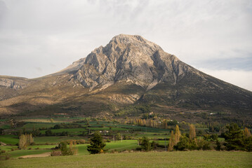 Fototapeta premium Panoramic view of a countryside landscape with very green grass, vegetation and in the background a large rocky mountain in the province of Huesca in Aragon during a cloudy day.