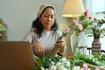 Attractive senior female florist creating beautiful bouquet with different flowers her floral shop