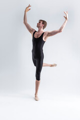 Sports Ideas. Young Athletic Caucasian Ballet Dancer Man Posing in Dancing Stretching Pose With Hands Lifted Up in Black Tights On White.