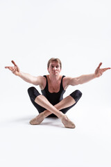 Obraz premium Ballerino Dancer Sitting While Practising Legs and Arms Forward Stretching Exercices Before Training In Black Sportive Tights in Studio.