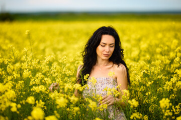 Naklejka na ściany i meble portrait of a brunette woman in a rapeseed field in spring