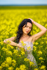 Naklejka na ściany i meble portrait of a brunette woman in a rapeseed field in spring