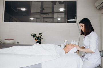 Obraz premium spa, resort, beauty and health concept - beautiful woman in spa salon getting face treatment.