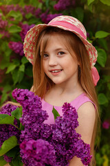 Fototapeta premium a beautiful blonde girl with long hair in a hat holds a bouquet of lilacs in her hands