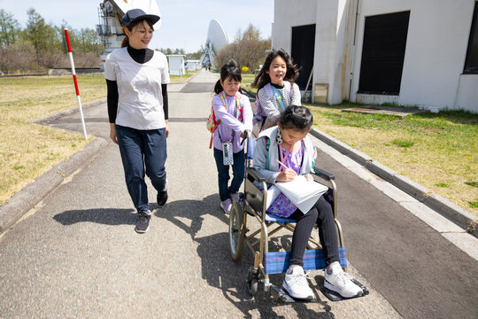 車いすに乗った女の子と学校の遠足に行く小学生の友達