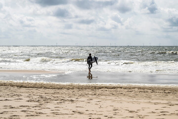 A surfer goes to the sea with a surfboard. Ride the waves on a surfboard. Seascape with a beach on the North Sea in the Netherlands.