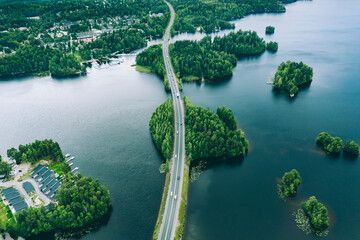 Aerial view of road bridge with cars between green forests and blue lakes in rural Finland